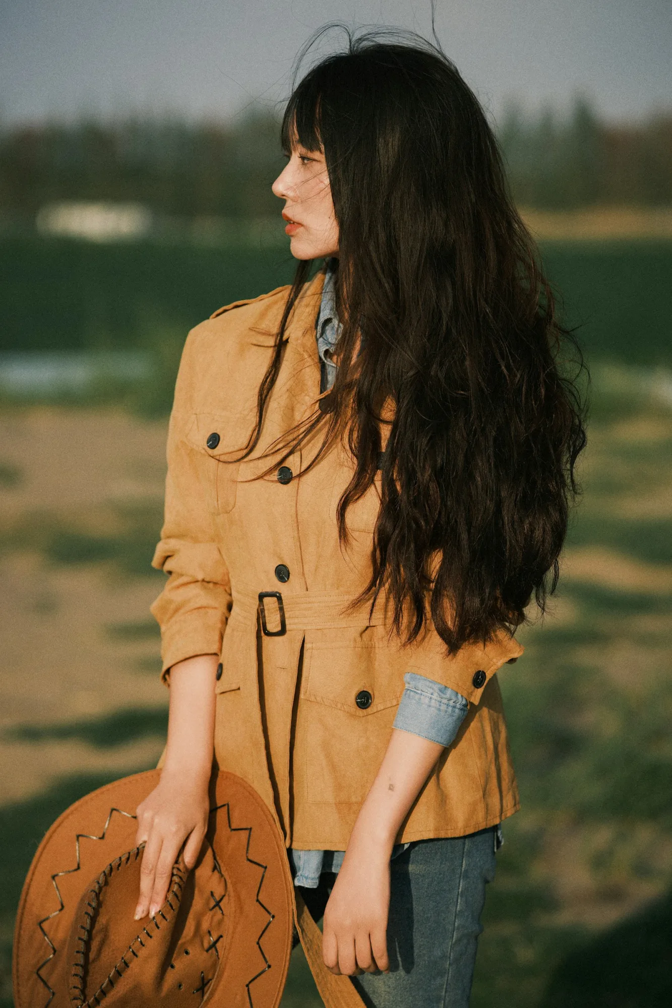 Tan suede coat styled with dark denim, back view in a field