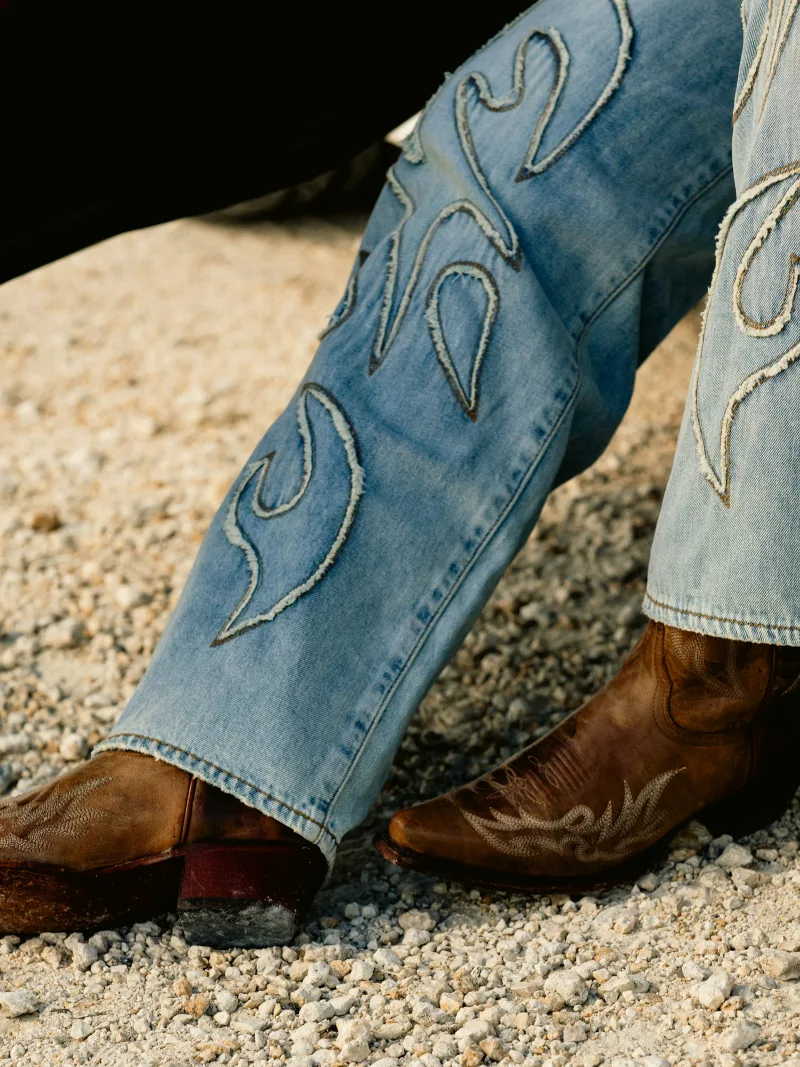 Embroidered boot-cut jeans stacked over tooled western boots