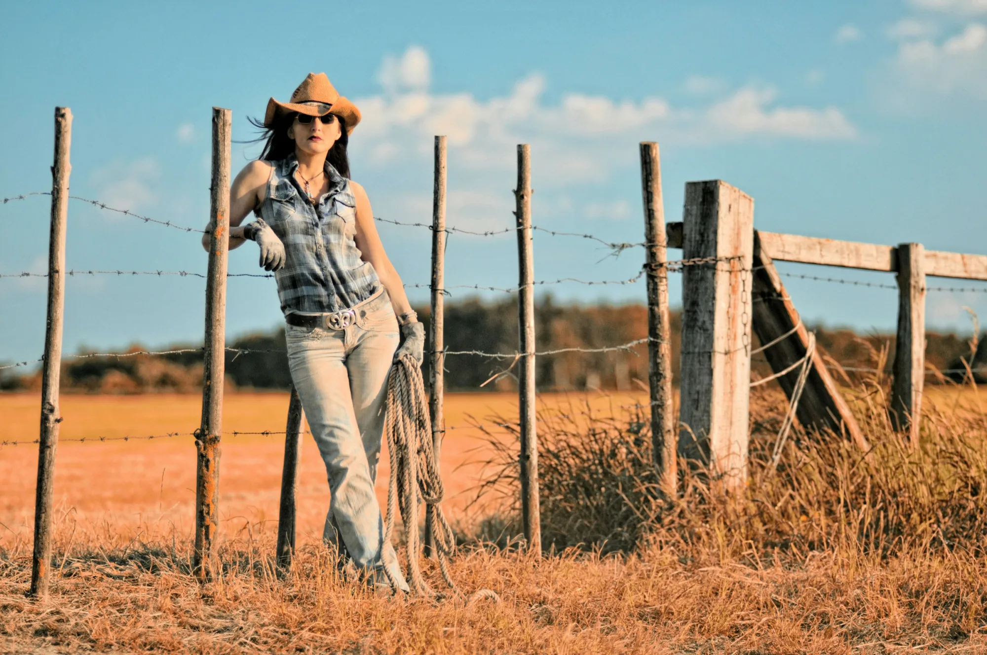 Cowgirl leaning on a ranch fence at golden hour